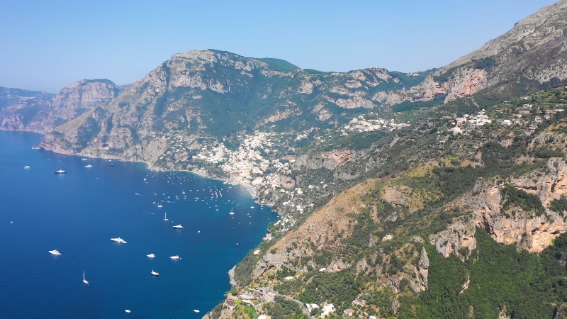 Aerial view of the Amalfi Coast with steep cliffs, villages, and boats scattered across the blue sea